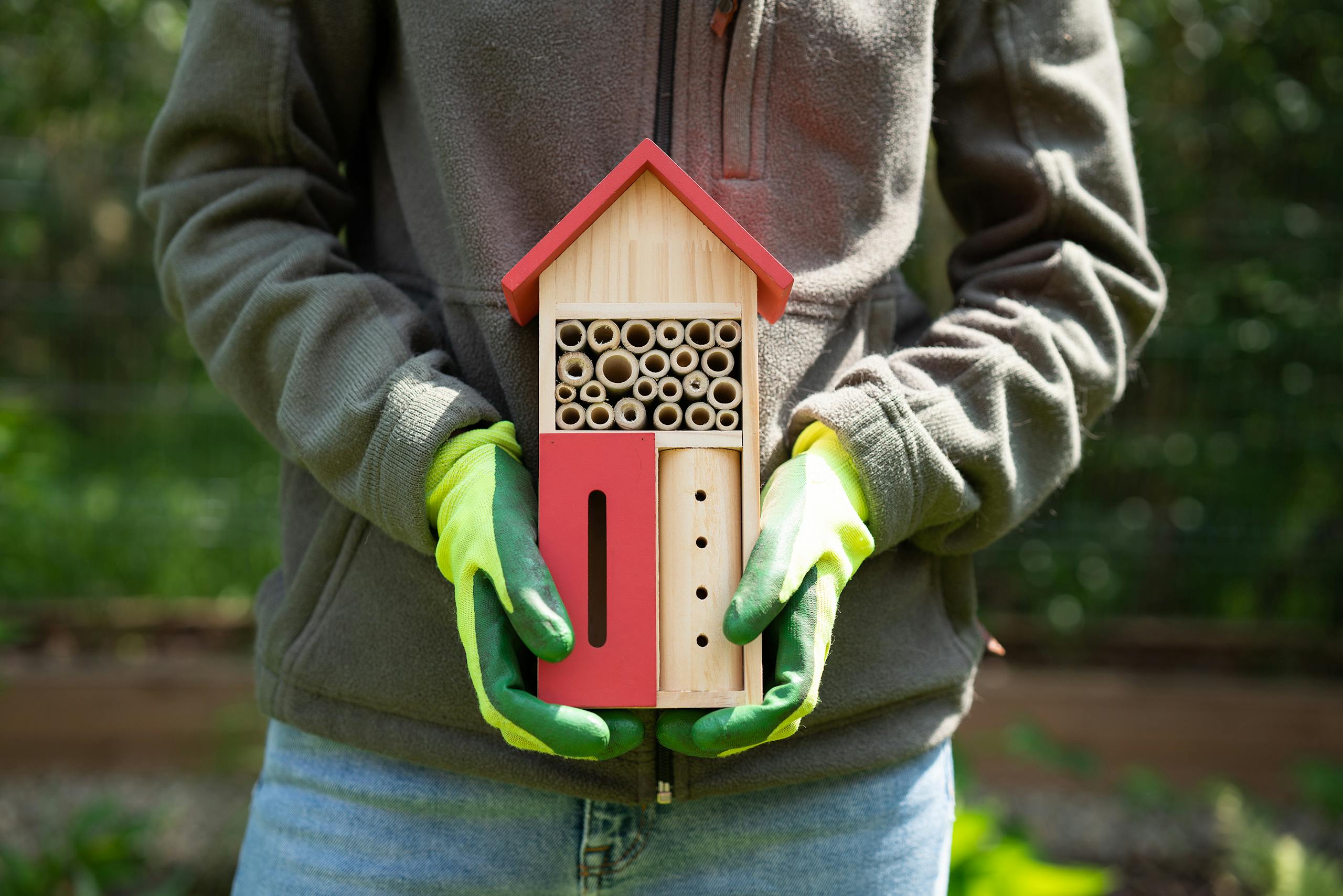 Hands holding a wooden bee hotel, promoting eco-friendly bee habitats.